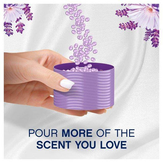 Hand pouring Lenor In-Wash Scent Booster purple beads into a container on soft white fabric.