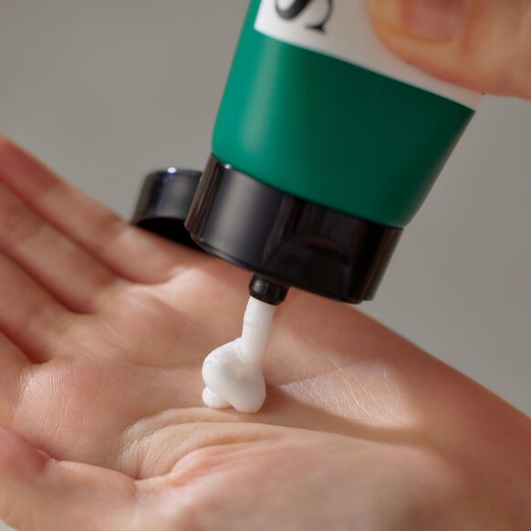 Green and black pump applying white cream to a hand