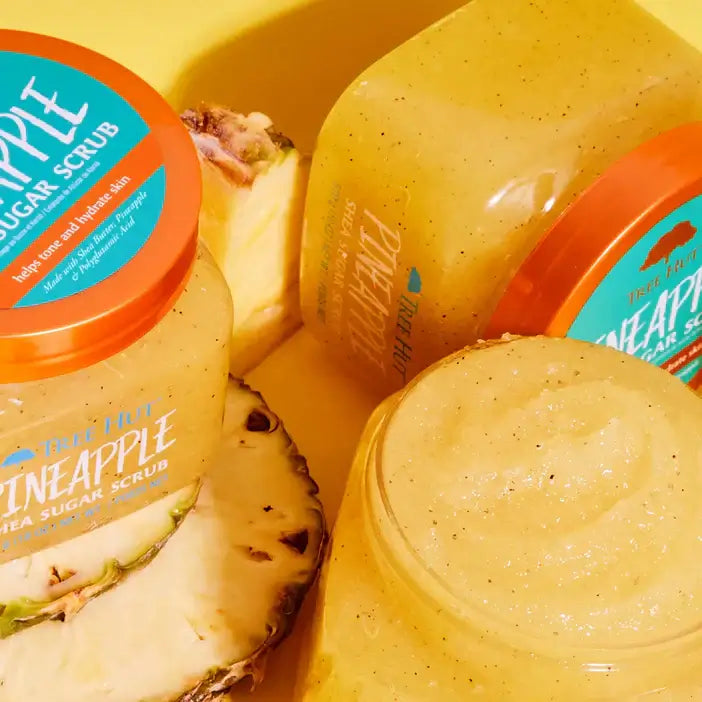 Jars of TREE HUT pineapple sugar scrub with a pineapple slice on a yellow background