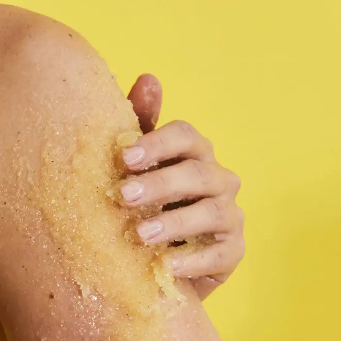 Hand using a TREE HUT Pineapple Sugar Scrub to scrub skin on a yellow background