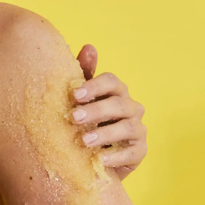 Hand using a TREE HUT Pineapple Sugar Scrub to scrub skin on a yellow background