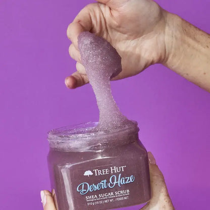 Hand holding a jar of Tree Hut Desert Haze Shea Sugar Scrub against a purple background