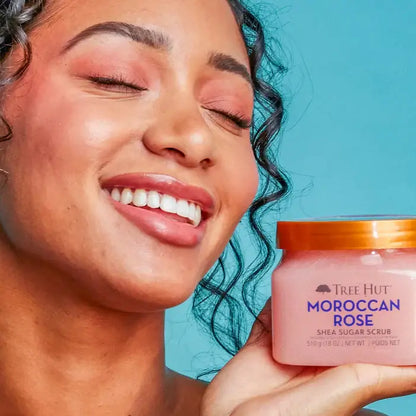 Smiling person holding TREE HUT Moroccan Rose Shea Sugar Scrub, showcasing radiant skin and a luxurious product.
