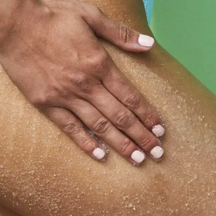 Hand with light nail polish touching a person's leg with TREE HUT Sugar Scrub Exotic Bloom