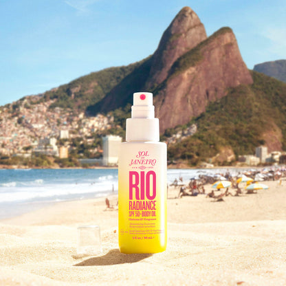 Sol de Janeiro Rio Radiance Oil SPF 50 90ml on a sandy beach with mountains in the background, perfect for sun protection.