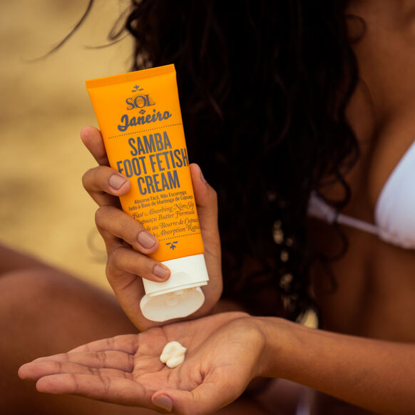 Sol de Janeiro Samba 2-Step Foot Fetish Care 90ml cream applied to hand with person in beach setting.