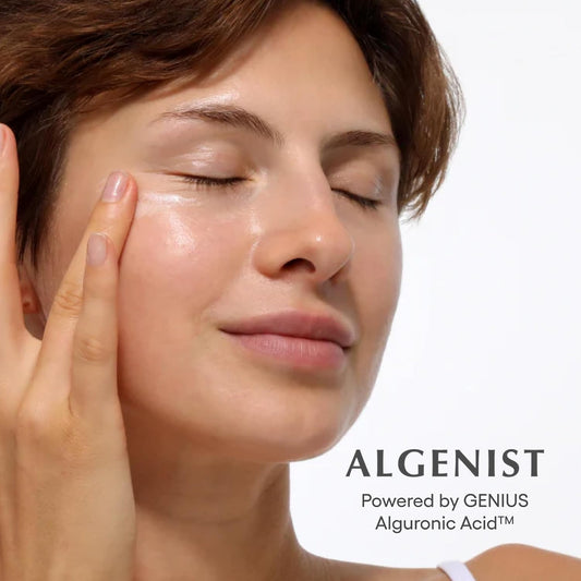 Woman applying cream to her face with 'Algenist' branding in the background