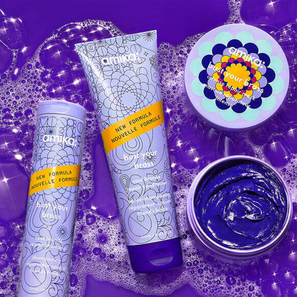 Amika Bust Your Brass hair care products with vibrant purple packaging and bubbles, designed for cool-toned blonde hair.