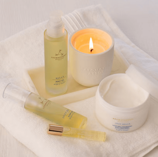 Aromatherapy Associates Deep Relax Sleep Mist, body oil, cream, and candle on a soft towel for ultimate relaxation.