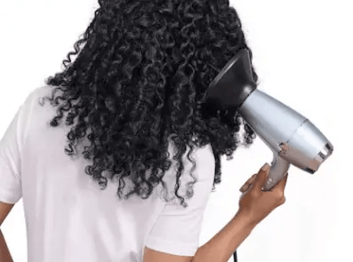 Woman using BaByliss Hydro-Fusion Anti-Frizz hair dryer on curly hair for smooth and shiny results.