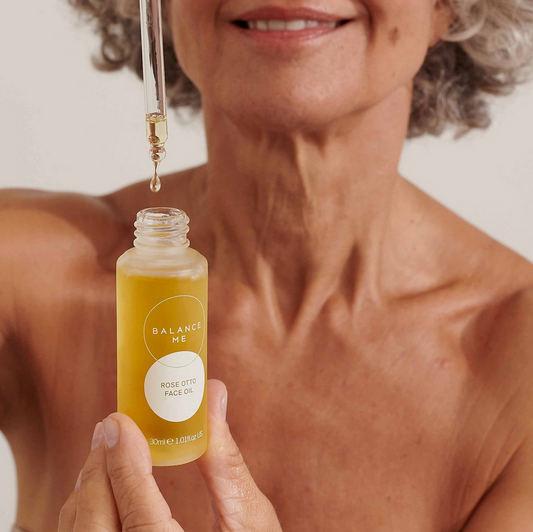 Woman holding a bottle of Balance Me rose otto face oil with a dropper.