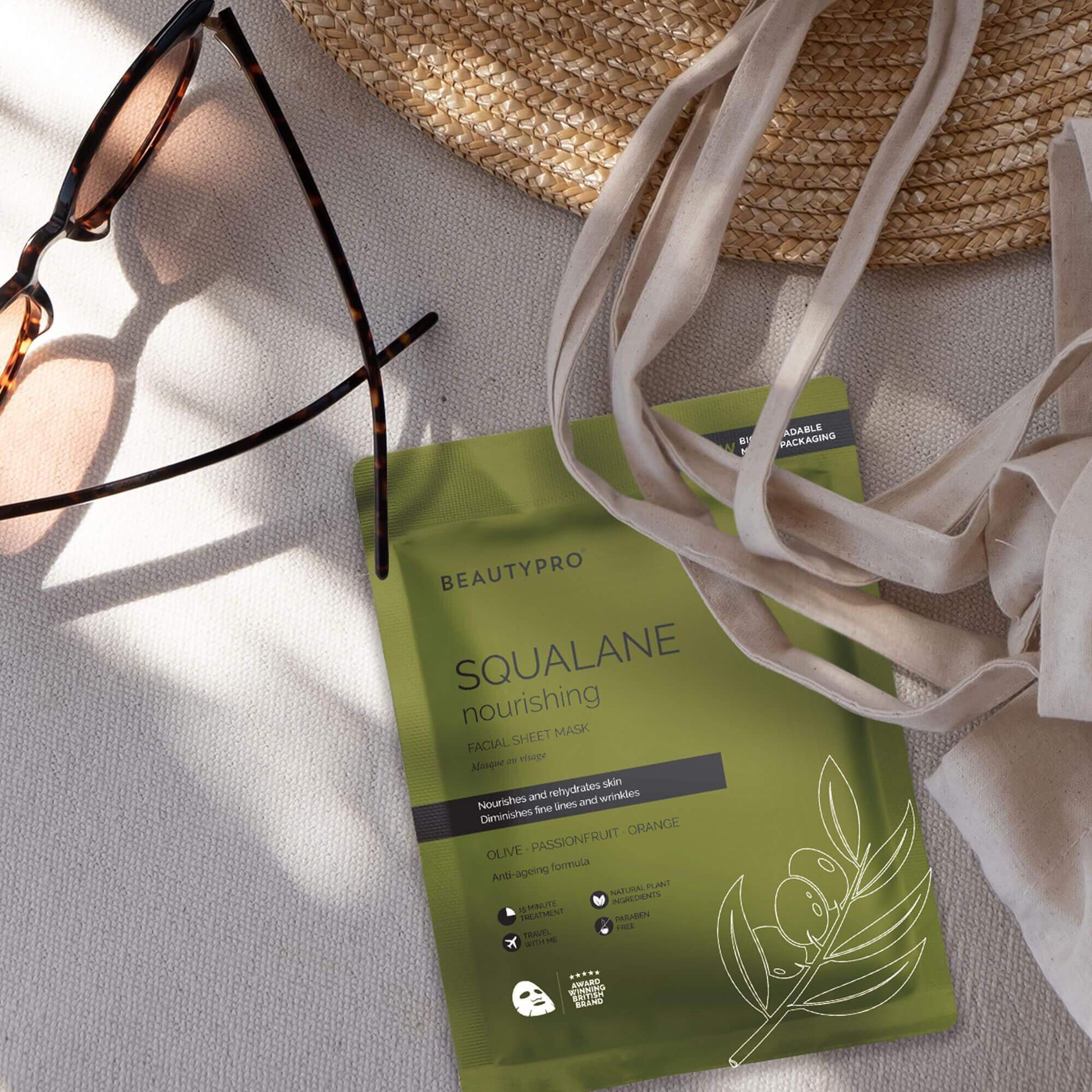 BeautyPro SQUALANE Nourishing Facial Sheet Mask on a table with sunglasses and a straw hat, promoting radiant skin.