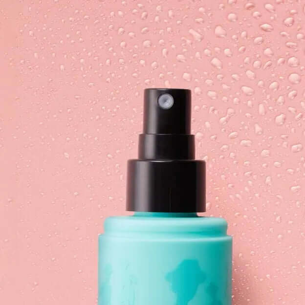 Benefit The POREfessional Super Setter Setting Spray in turquoise bottle against a pink backdrop with water droplets.