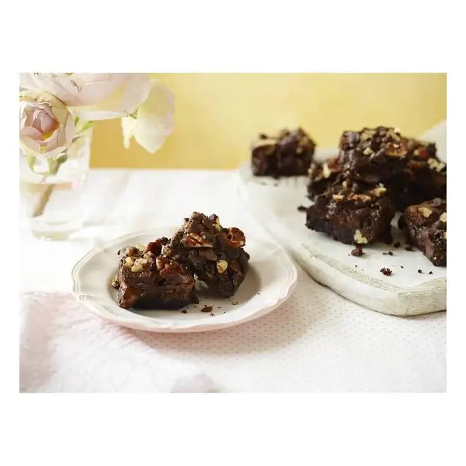 Delicious chocolate fudge brownies topped with nuts served on a plate with fresh flowers in a vase.