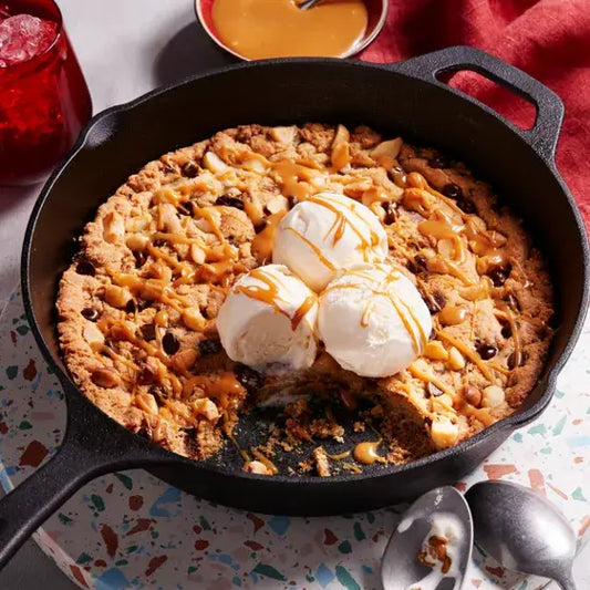 Warm chocolate chip cookie skillet topped with ice cream and caramel sauce, served in a cast iron pan.
