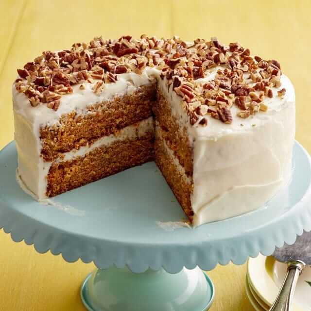 Delicious carrot cake decorated with cream cheese icing and topped with pecans on a teal cake stand.