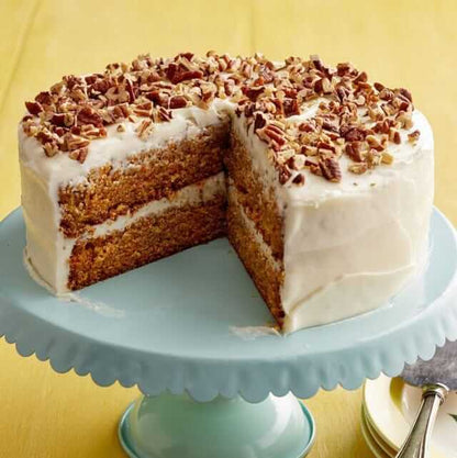 Delicious carrot cake decorated with cream cheese icing and topped with pecans on a teal cake stand.
