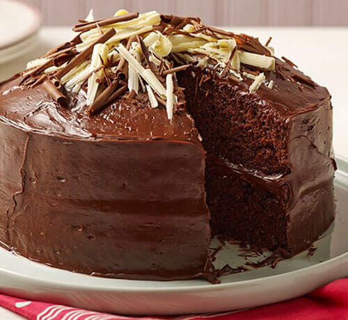 Rich chocolate cake with smooth frosting and white chocolate shavings on top, showcasing a slice removed.