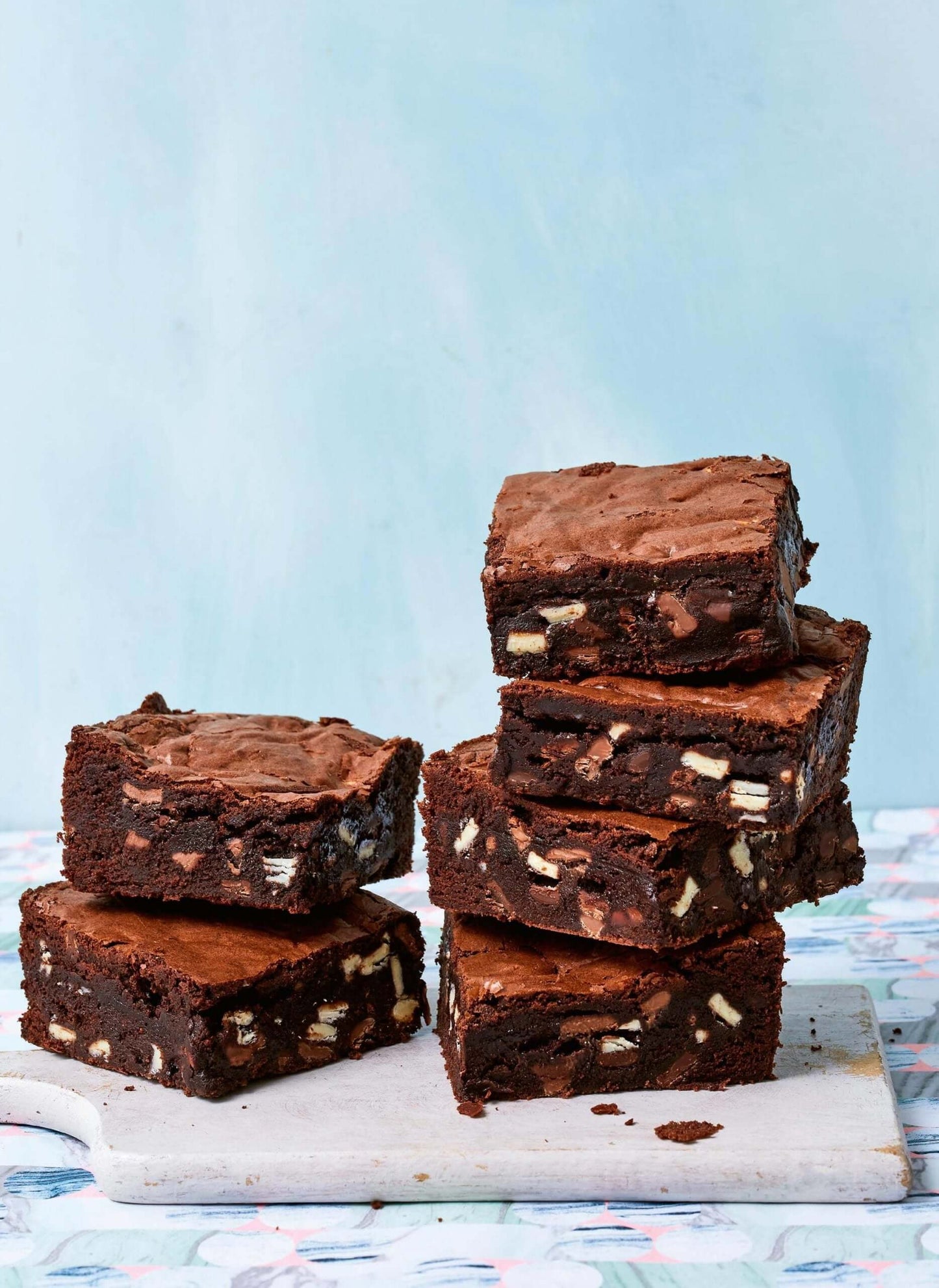 Stack of rich, fudgy brownies packed with chocolate chunks on a cutting board.