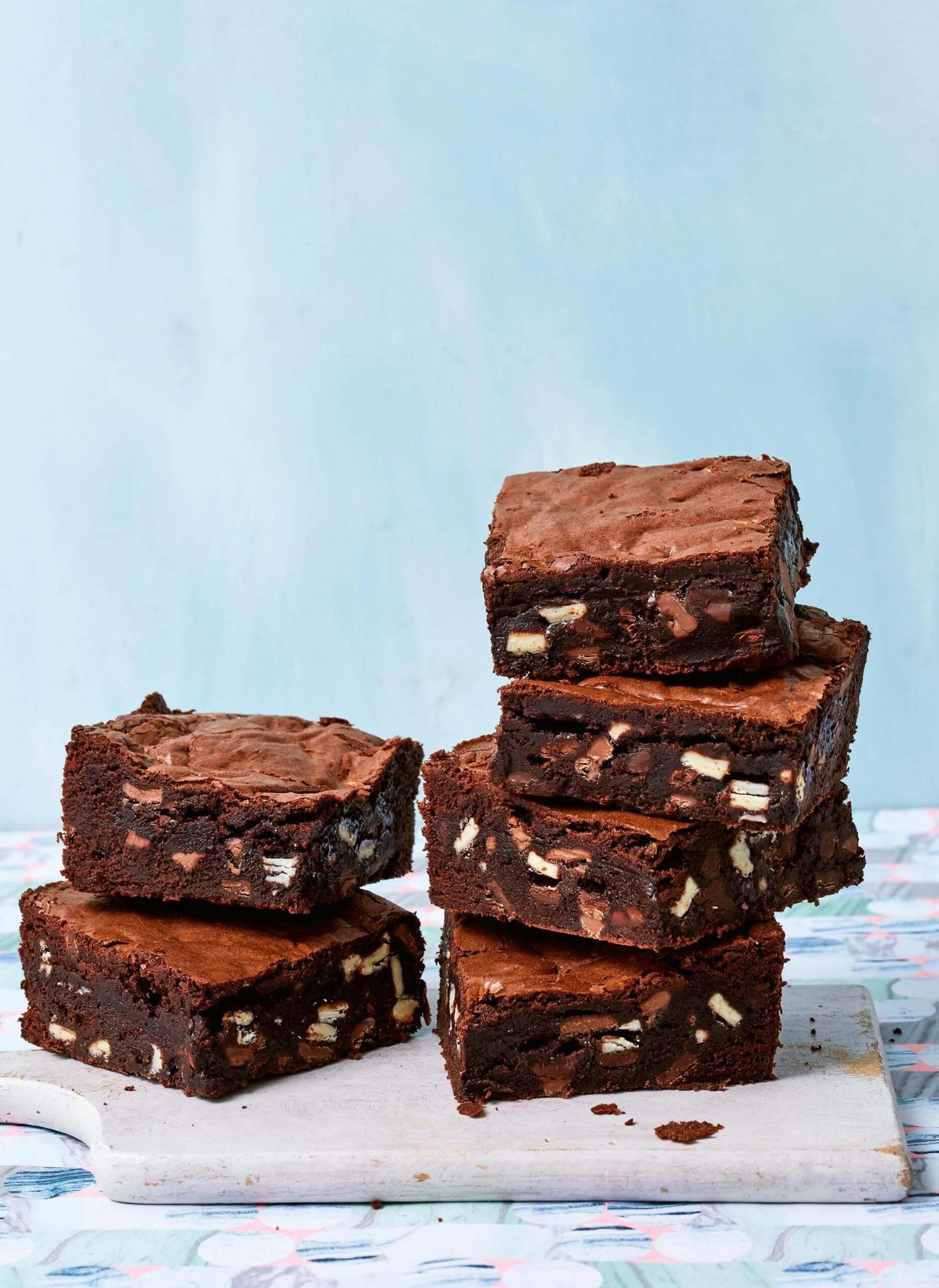Stack of rich, fudgy brownies packed with chocolate chunks on a cutting board.