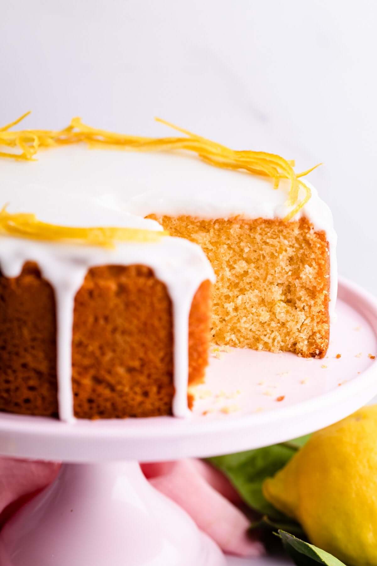 Moist Betty Crocker Zesty Lemon Cake with icing and lemon garnish on a pink cake stand.