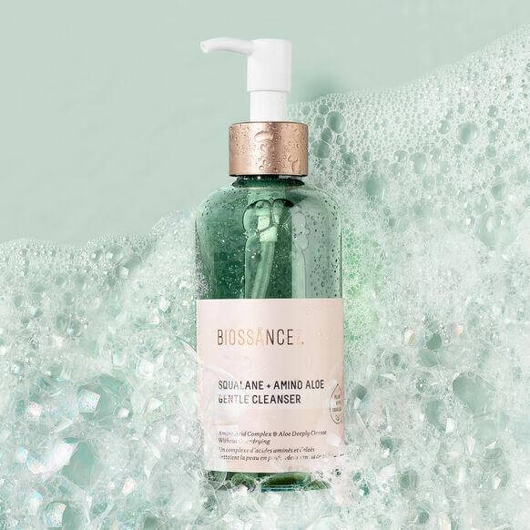 BIOSSANCE Squalane + Amino Aloe Gentle Cleanser in a pump bottle amidst bubbles on a soft green background.