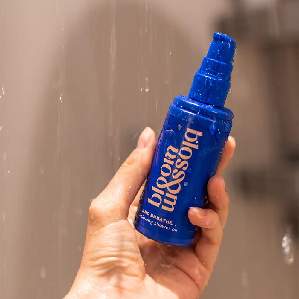 Bloom & Blossom Hand holding a blue bottle of 'bloom & breathe' shower oil against a shower background.