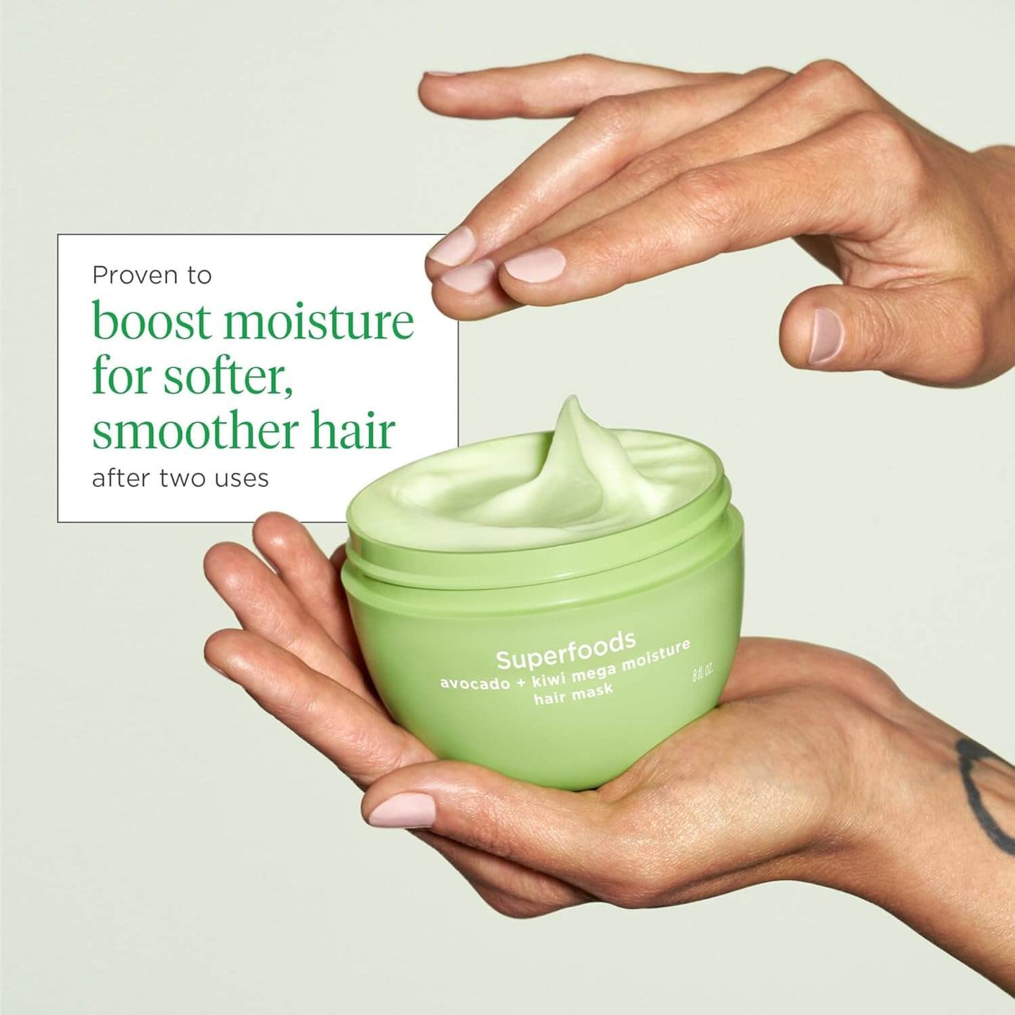 Briogeo Green jar of Superfoods hair mask held by a hand with text about hair benefits.
