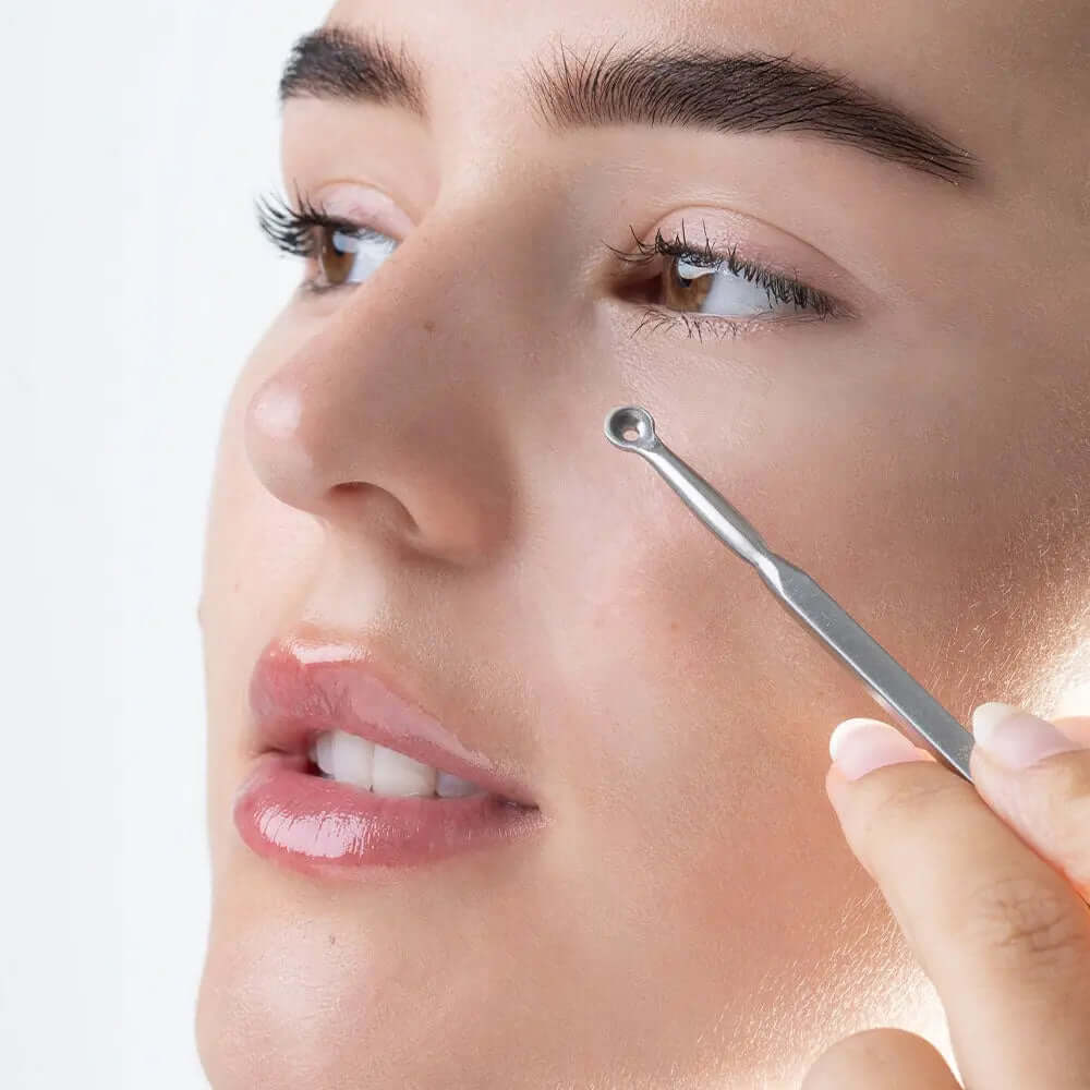 Close-up of a woman using a stainless steel blackhead remover tool on her face.