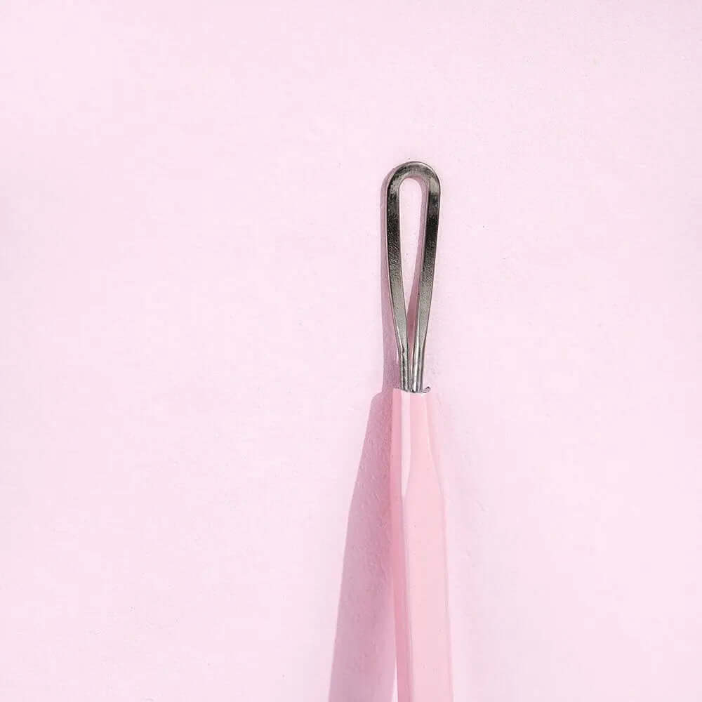 Brushworks Black Head Removal Tool with ergonomic design for effective blackhead removal, shown against a pink background.