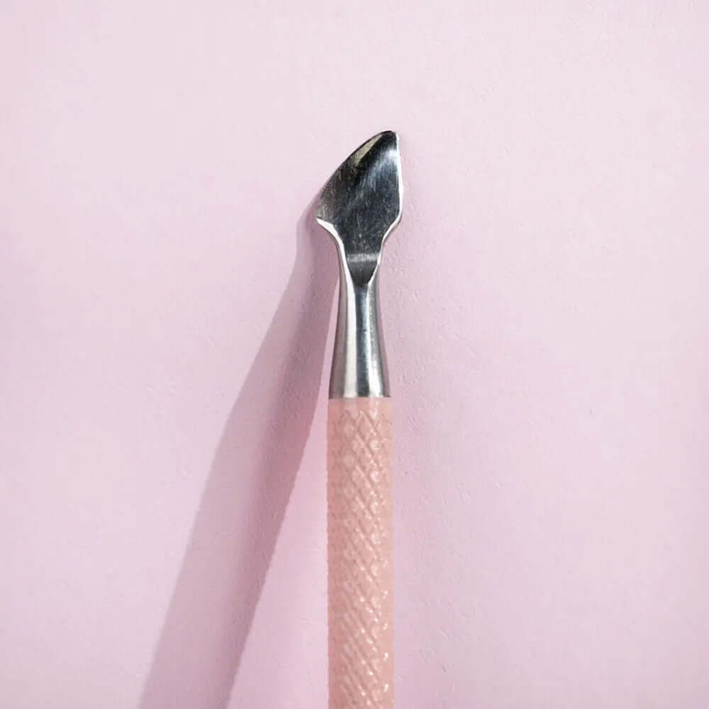 Brushworks Cuticle Pusher tool with pink handle, featuring a curved spoon end for cuticle care and nail cleaning.