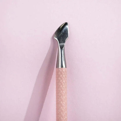 Brushworks Cuticle Pusher tool with pink handle, featuring a curved spoon end for cuticle care and nail cleaning.