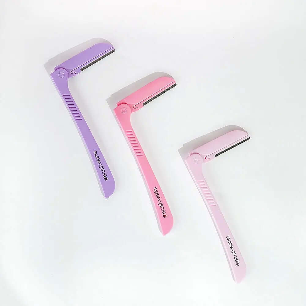 Brushworks Eyebrow Razors in pink and purple, designed for painless eyebrow shaping and gentle exfoliation.