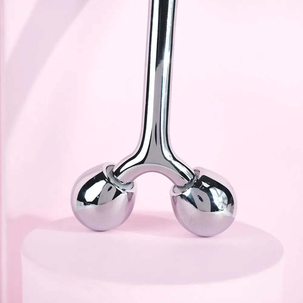 Brushworks Face Sculpting Zinc Roller with chrome balls for facial massage on pink background.