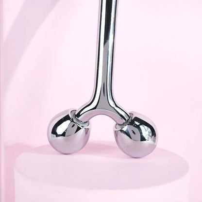Brushworks Face Sculpting Zinc Roller with chrome balls for facial massage on pink background.