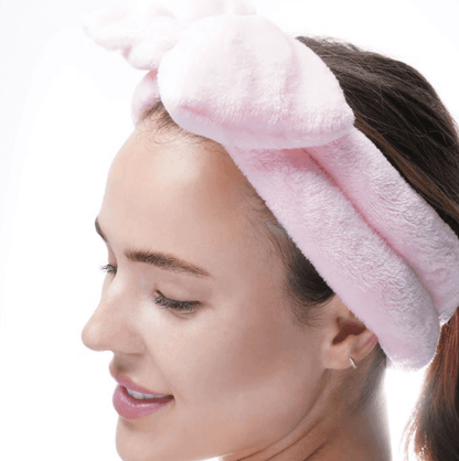 Close-up of a woman wearing a pink Brushworks Makeup Headband with a bow, perfect for skincare and makeup routines.