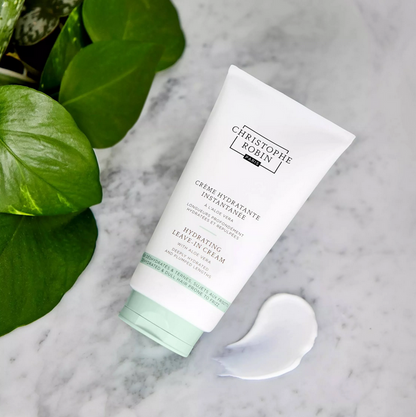 Tube of Christophe Robin cream on a marble surface with green leaves.