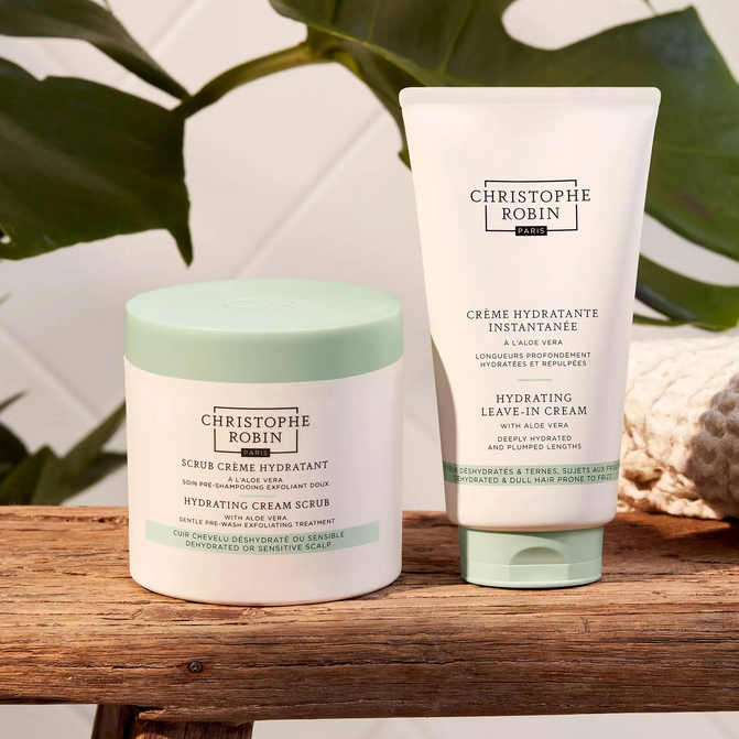 Two skincare products by Christophe Robin on a wooden surface with a leafy background