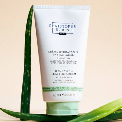 Tube of Christophe Robin hydrating leave-in cream with aloe vera leaves on a beige background