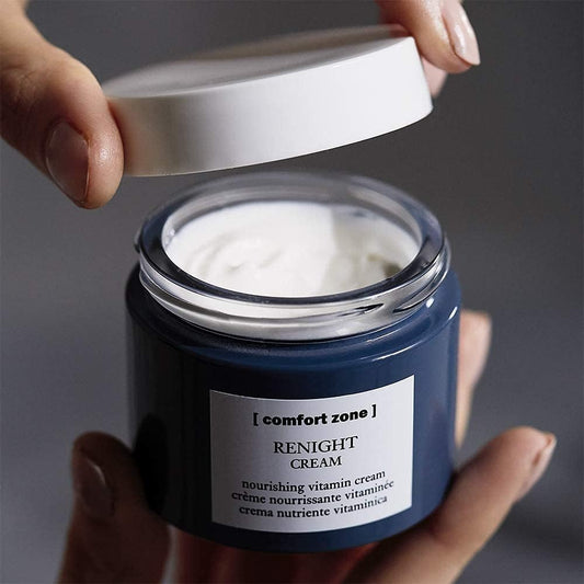 Blue jar of 'Renight Cream' by 'Comfort Zone' with a hand opening it on a gray background