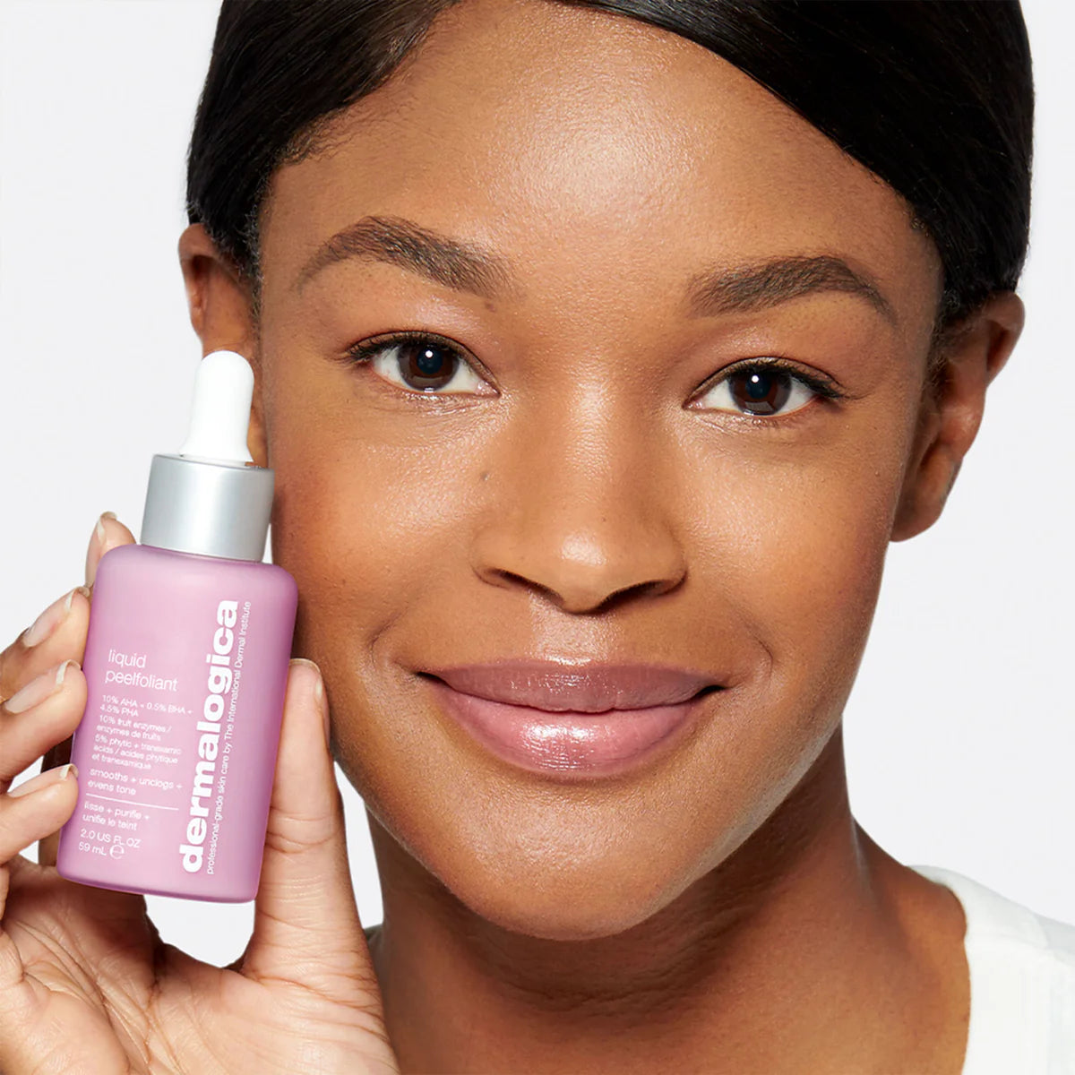 Woman holding a pink bottle of Dermalogica product against a white background