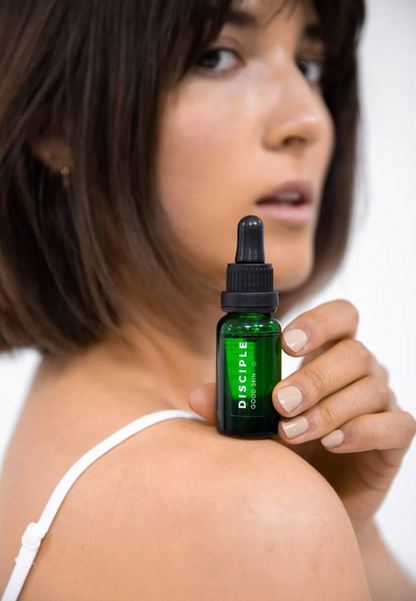 Woman holding a bottle of Disciple skincare product on a white background