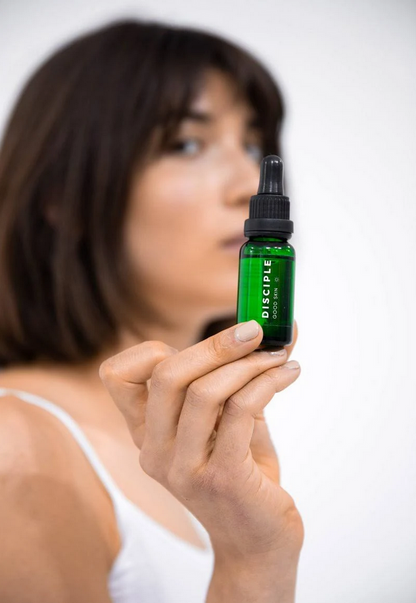 Woman holding a green bottle labeled 'Disciple' against a white background
