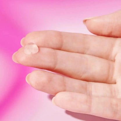Close-up of a hand holding a drop of Drunk Elephant T.L.C. Framboos™ Glycolic Night Serum against a pink background.