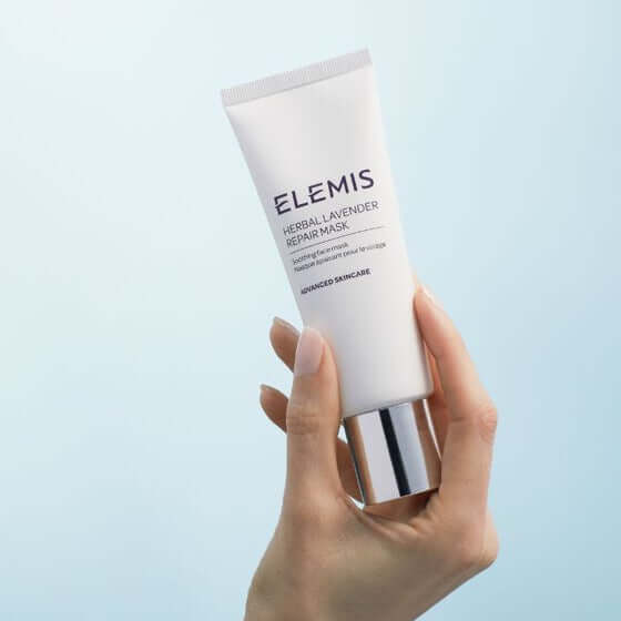 Hand holding a tube of Elemis Herbal Lavender Repair Mask against a light blue background