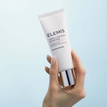Hand holding a tube of Elemis Herbal Lavender Repair Mask against a light blue background