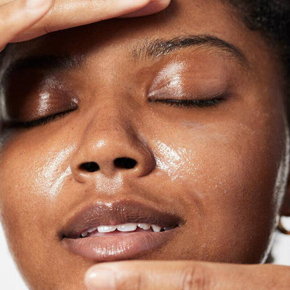 Close-up of a person with clean, glowing skin applying a skincare product to their face.