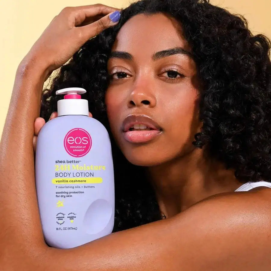 Woman holding an eos body lotion bottle against a beige background