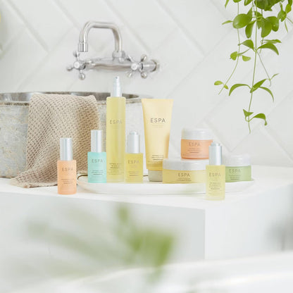Collection of ESPA products on a bathroom counter with a bathtub and plant in the background.