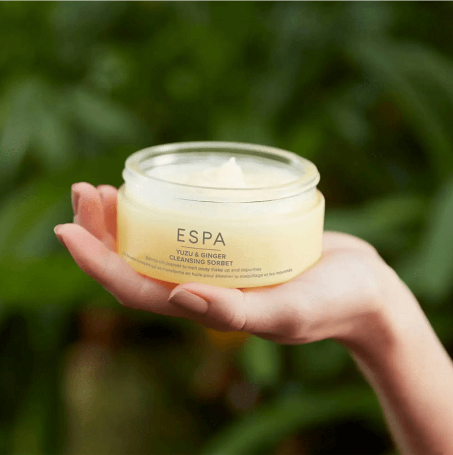 Hand holding a jar of ESPA product against a blurred green background
